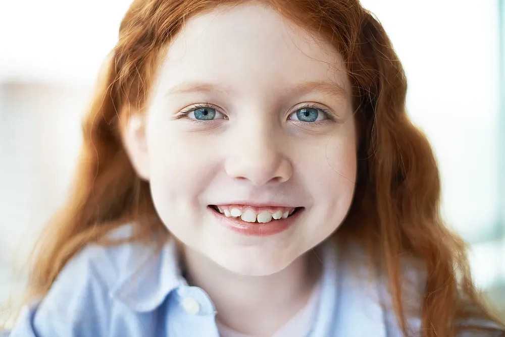 Mädchen mit nachdenklichem Blick neben einer Darstellung von Platzmangel und eng stehenden Zähnen im Kindergebiss.